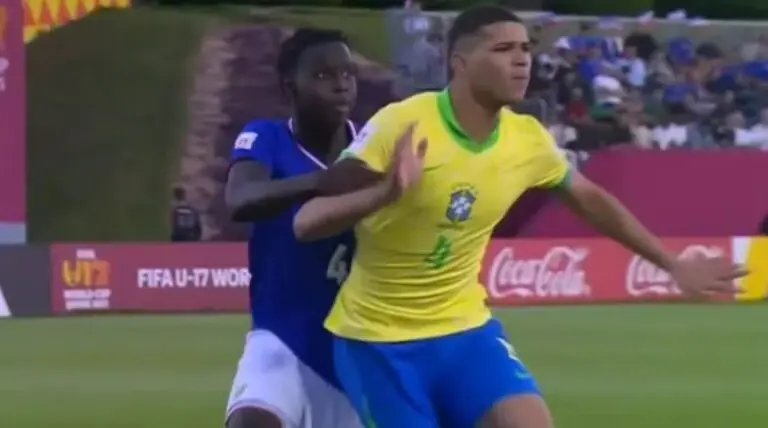 Uma decisão da arbitragem, mantida após consulta ao árbitro de vídeo (VAR), gerou intensa controvérsia e revolta de torcedores durante a partida entre a Seleção Brasileira e a França, válida pelas oitavas de final da Copa do Mundo Sub-17. O lance, que resultou no gol francês, colocou o time canarinho em desvantagem no placar. O confronto terminou empatado em 1 a 1 no tempo regulamentar, com o Brasil garantindo a vaga nas quartas de final após uma emocionante disputa de pênaltis, onde o goleiro João Pedro, do Santos, se destacou. O jogo ocorreu nesta terça-feira (18) no complexo esportivo Aspire Zone, em Doha, no Catar. A vitória suada por 4 a 3 nas penalidades, após o empate com gols de Rémi Himbert, para a França, e Pietro Tavares, para o Brasil, garantiu ao time comandado por Carlos Eduardo Patetuci a permanência na busca pelo pentacampeonato mundial da categoria. O lance polêmico que abriu o placar no jogo Aos 30 minutos da primeira etapa, o árbitro assinalou uma penalidade máxima contra a equipe brasileira em um lance envolvendo o goleiro João Pedro e o jogador francês. A comissão técnica da seleção solicitou a revisão do lance, argumentando que o arqueiro havia tocado primeiro na bola. Mesmo após a checagem no monitor do VAR, a decisão inicial de campo foi mantida, irritando jogadores e a torcida brasileira que acompanhava a transmissão. A revolta dos torcedores foi imediatamente notada nas redes sociais, com diversas mensagens classificando a decisão como um "absurdo" e um "roubo" contra a equipe. Na cobrança, João Pedro conseguiu defender a batida de Batola, mas o atacante Himbert aproveitou o rebote para abrir o marcador para a França. Reação imediata nas plataformas digitais A manutenção da marcação do pênalti, mesmo com o recurso do VAR, foi o principal tema dos comentários de torcedores e jornalistas nas plataformas digitais. A discussão se concentrou na interpretação da jogada, que para muitos, não configurava infração suficiente para a penalidade. O descontentamento da torcida refletiu a pressão do jogo de mata-mata. A Seleção Brasileira, conhecida por sua campanha invicta na fase de grupos, encontrava-se em uma situação de desvantagem provocada por um erro de arbitragem, o que aumentou o drama da partida. Busca heroica pelo empate no segundo tempo Com o placar adverso, o time brasileiro voltou para o segundo tempo determinado a buscar a igualdade, exercendo forte pressão no campo adversário. A Seleção dominou as ações e criou diversas oportunidades, mas esbarrou na bem postada defesa francesa e em uma penalidade perdida. Aos 37 minutos da etapa final, o Brasil teve a chance de ouro para empatar com um pênalti marcado a seu favor, mas Ruan Pablo, em lance de grande frustração, acertou a trave. A persistência do ataque brasileiro foi recompensada aos 44 minutos, quando o meia Pietro Tavares, que havia entrado no decorrer do jogo, aproveitou um cruzamento na área. O chute preciso no ângulo do goleiro Jourdren decretou o empate em 1 a 1 e levou a partida para a decisão por pênaltis. João Pedro decide nos pênaltis mais uma vez A disputa de penalidades consolidou o goleiro João Pedro como o grande nome da classificação, repetindo o feito das oitavas de final contra o Paraguai, onde defendeu três cobranças. Na nova decisão, o arqueiro defendeu duas batidas francesas, de Camara e Leccese, garantindo o avanço da seleção. Os jogadores Dell, Luís Pacheco, Gabriel Mec e Ruan Pablo, que se redimiu da penalidade perdida no tempo normal, converteram suas cobranças. Com o placar final de 4 a 3 nas penalidades, o Brasil assegurou sua vaga na próxima fase. Caminho e próximo adversário da seleção canarinho Com a classificação garantida, a Seleção Brasileira se junta às oito melhores equipes da competição. O próximo desafio da equipe será nas quartas de final, quando enfrentará o vencedor do confronto entre Marrocos ou Mali, jogo que também acontece nesta terça-feira. Brasil x França no Mundial sub-17