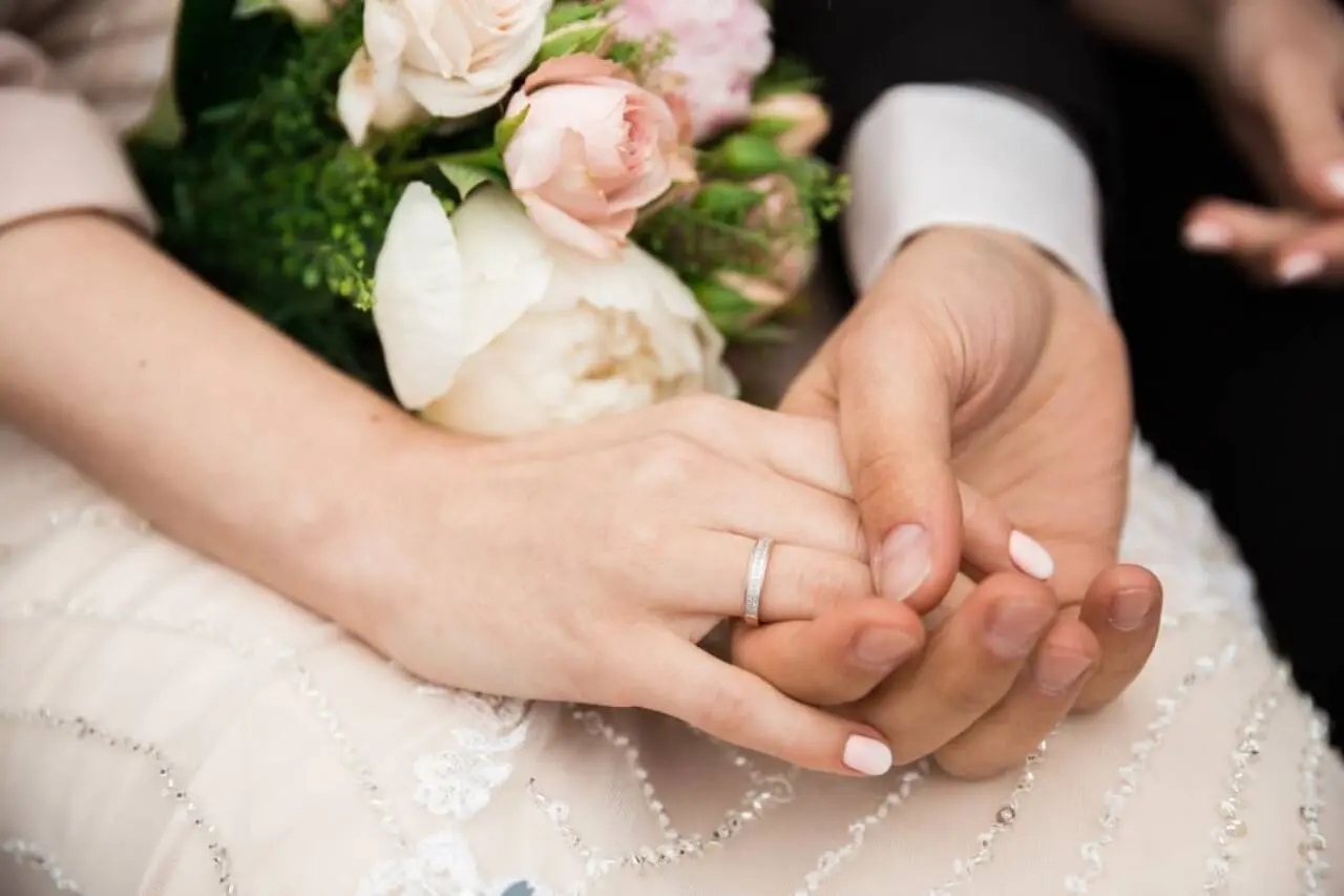 Mãos com alianças de casamento e flores