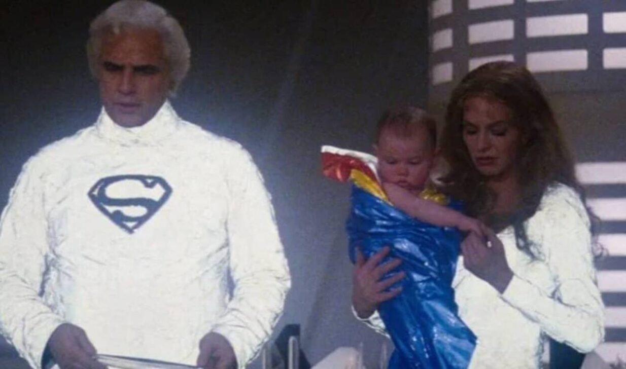 Marlon Brando's Jor-El stands next to Susannah York's Lara as she holds a young Kal-El in Superman - Warner Bros