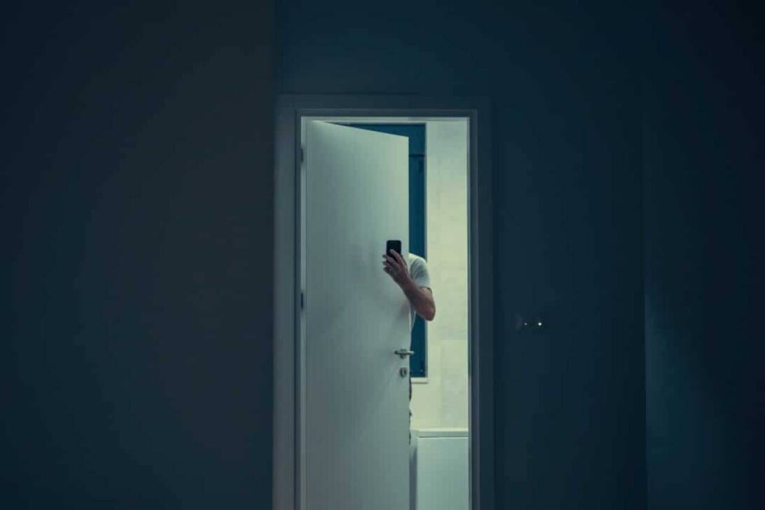 Homem escondido atrás da porta com celular.