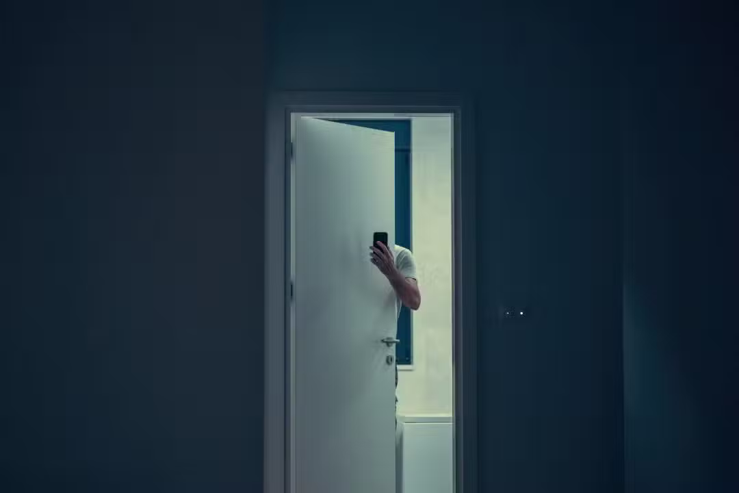 Homem escondido atrás da porta com celular.