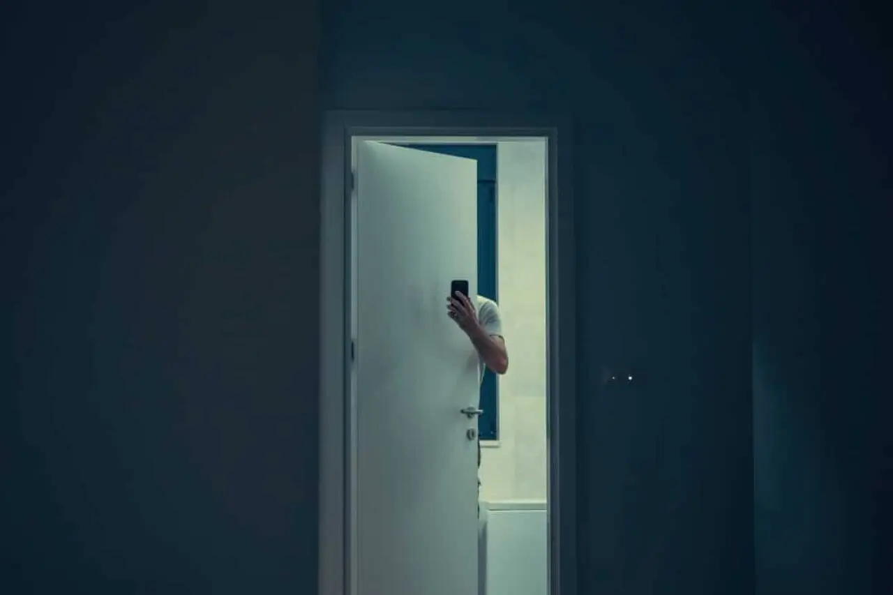 Homem escondido atrás da porta com celular.