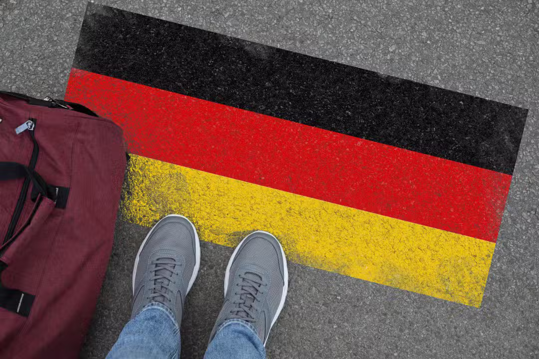 Imigração. Homem com bolsa em pé no asfalto perto da bandeira da Alemanha