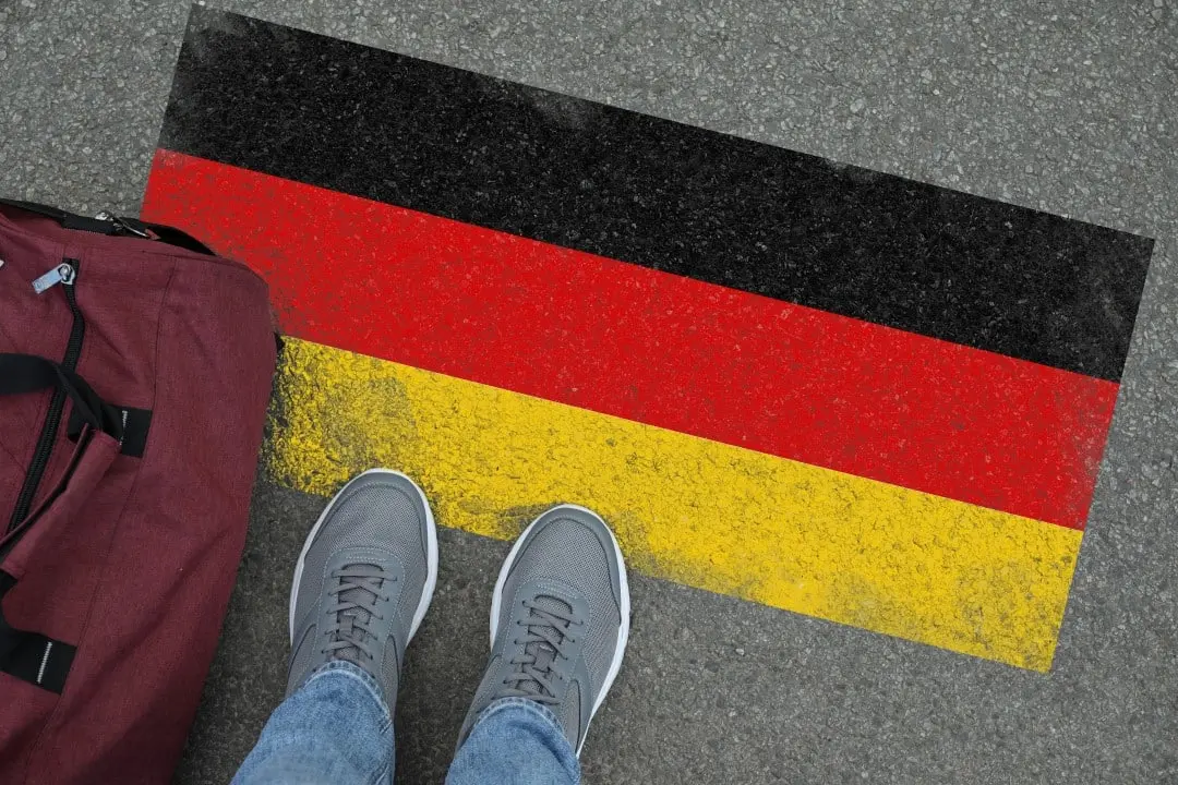 Imigração. Homem com bolsa em pé no asfalto perto da bandeira da Alemanha