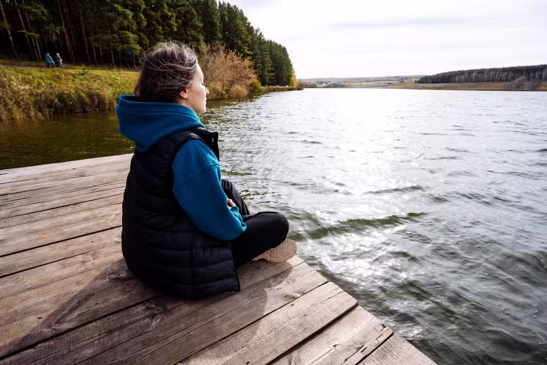 Mulher sentada em frente a um lago pensativa, reflexão, quieta