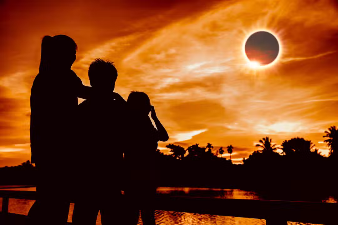 Silhuetas de três pessoas olhando para o eclipse solar total