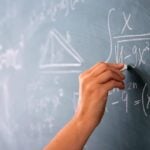 mão segurando giz, equações matemáticas no quadro, professor