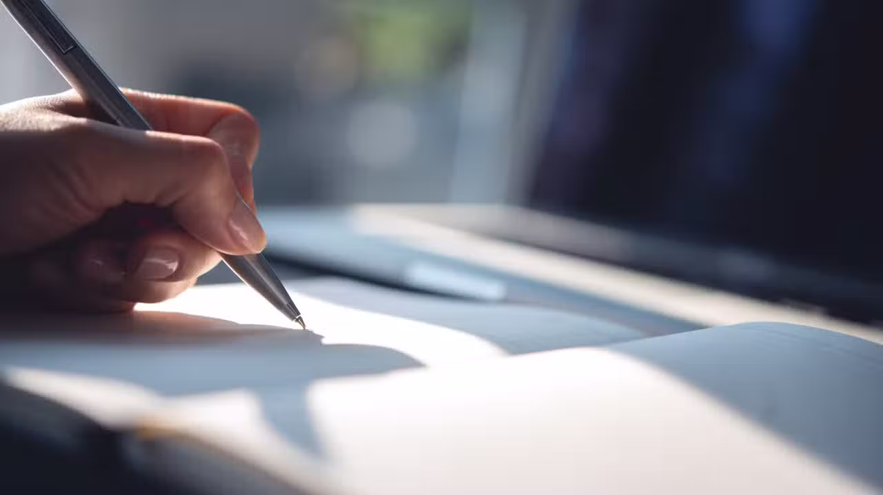 Mão segurando caneta, escrevendo, papel