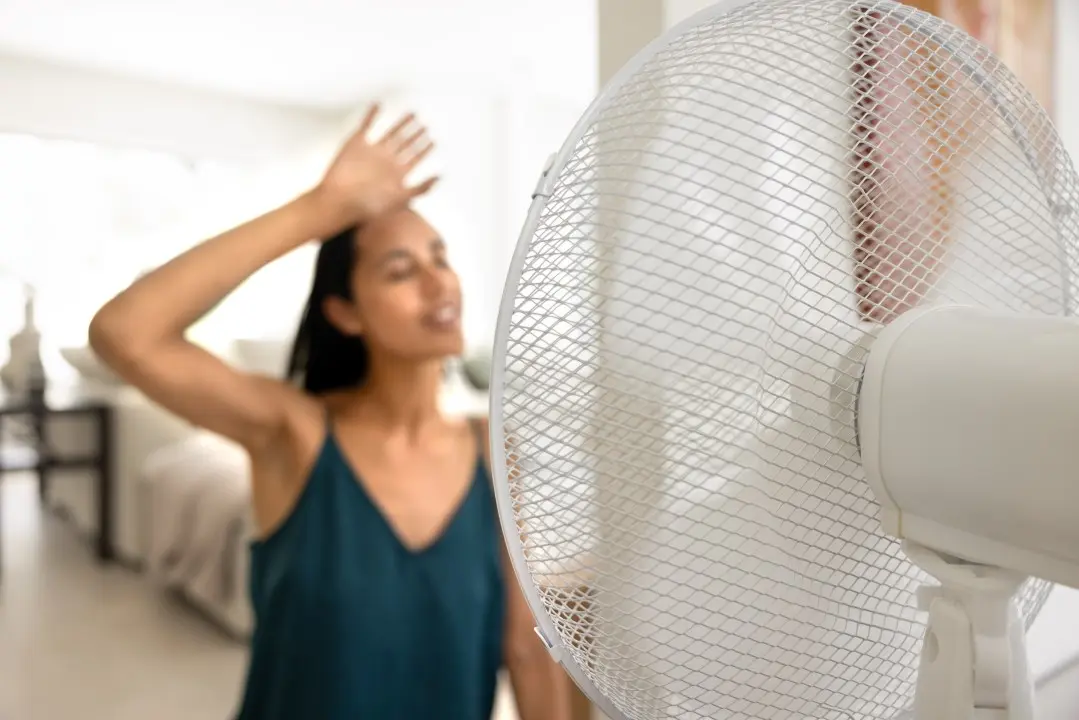 Mulher com a mão na testa em frente ao ventilador, calor