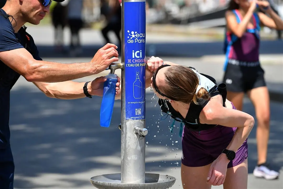 Pessoas bebendo água na fonte pública nas margens do rio Sena, na França, calor