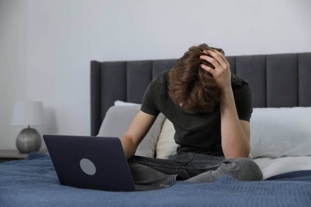 Menino triste com notebook na cama