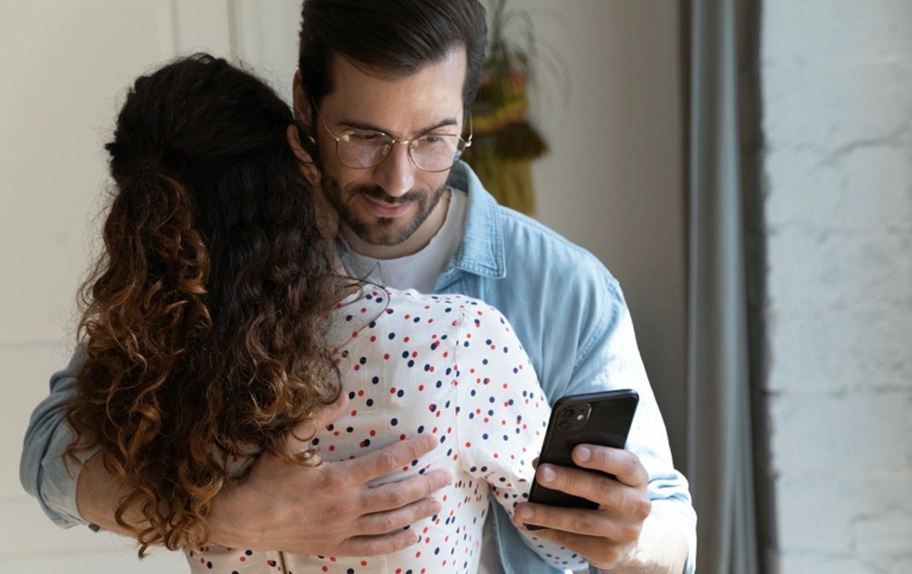 Homem abraçando mulher e olhando celular, casal, conceito de infidelidade, traição - fizkes/Shutterstock.com