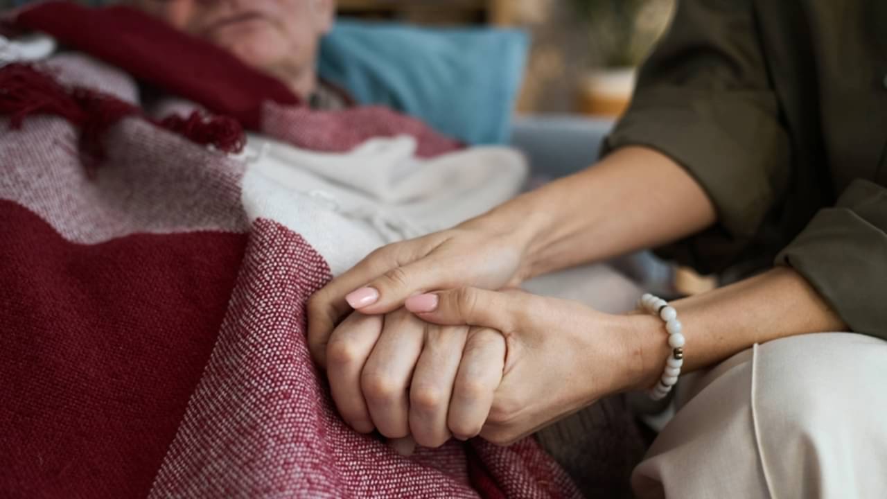 Homem idoso acamado, auxílio-doença, mulher segurando mão de idoso - DragonImages/istockphoto.com
