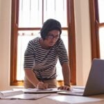 Mulher em pé à sua mesa, trabalhando, conceito de empreendedor MEI - PeopleImages/Shutterstock.com