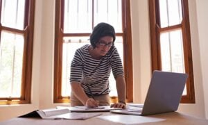 Mulher em p&eacute; &agrave; sua mesa, trabalhando, conceito de empreendedor MEI - PeopleImages/Shutterstock.com