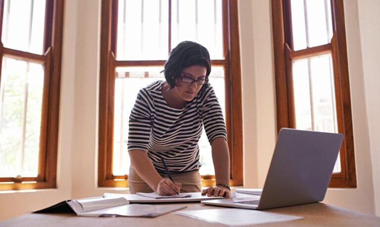 Mulher em pé à sua mesa, trabalhando, conceito de empreendedor MEI - PeopleImages/Shutterstock.com