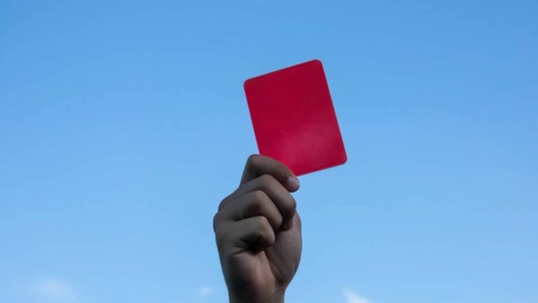 Mão do árbitro segurando cartão vermelho - MihailDechev/ istockphoto.com